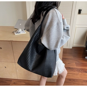 Detail shot of the black woven leather tote bag texture on model in an indoor setting