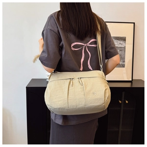 Close-up of cream nylon crossbody bag featuring dual front zippers and silver round logo