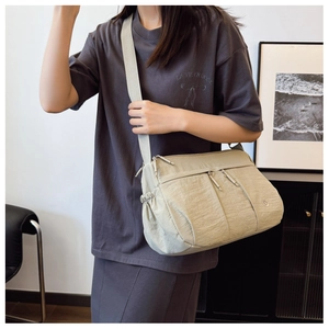 Detail of beige nylon crossbody bag featuring multiple zipper pockets and wide shoulder strap