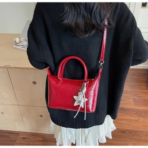 Borsa rossa lucida a pieghe con ciondolo a stella indossata su un maglione nero