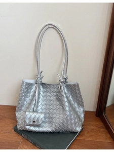 Silver woven tote bag with a matching mini pouch on a decorative book in home setting