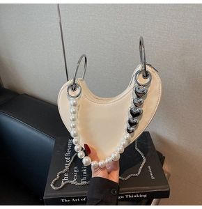 Dettaglio della borsa bianca a forma di cuore con catena di perle e manico argento