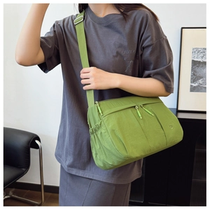 Detail shot of a green nylon crossbody bag showing the dual zipper pockets and side pocket