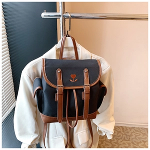 Detail of vintage canvas backpack with heart embroidery and brown leather trim on white coat