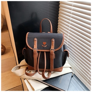 Detail of canvas backpack featuring floral embroidery and brown leather buckles