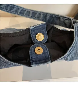 Detailed macro view of the gold magnetic closure on a blue denim tote bag lining