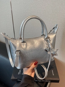 Borsa a tracolla a pieghe argento con ciondoli metallici su sfondo di libro nero