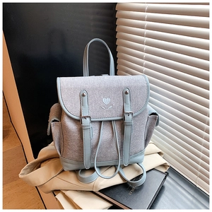 Close-up of small blue canvas backpack with heart embroidery and leather buckle straps