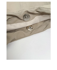 Detailed close-up of a silver magnetic snap closure on light beige nylon tote bag