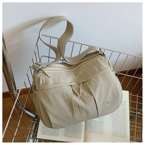 Close-up of lightweight khaki nylon crossbody bag with multiple zippers in a silver cart