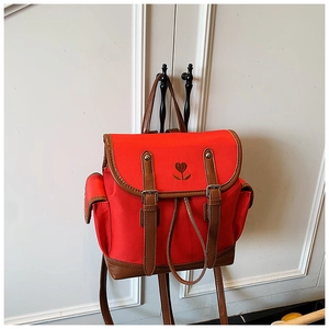 Detail of red canvas backpack featuring heart embroidery and brown leather trim accents