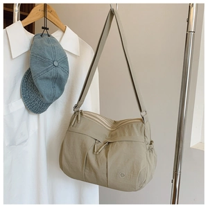 Detail of light khaki nylon shoulder bag featuring multiple zippers and side drawstring