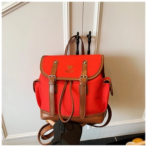 Detail of red backpack featuring floral embroidery and brown leather trim accents