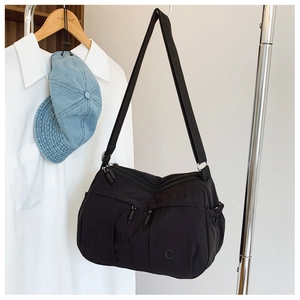 Close-up of black nylon crossbody bag with multi-zipper pockets on a wooden hanger