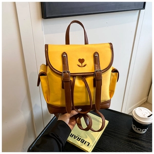 Detail of yellow canvas backpack featuring heart floral embroidery and brown leather straps