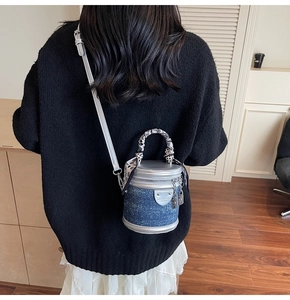 Détail d'un sac seau cylindrique en denim bleu avec finitions en cuir argenté et foulard