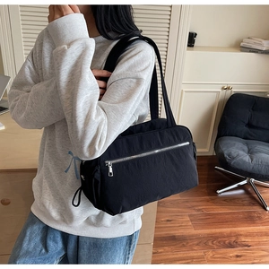 Detail of black nylon tote bag with silver zipper and front pocket on shoulder