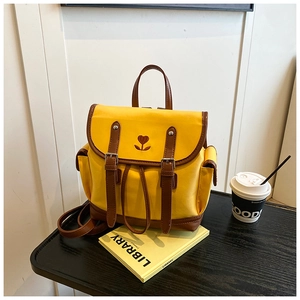 Detail of yellow canvas backpack showing heart embroidery and brown leather strap closure