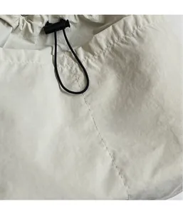 Détail d'un sac cabas beige clair avec un cordon de serrage noir et un bouton d'arrêt