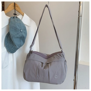 Close-up of lightweight grey nylon crossbody bag hanging with multi-pocket zipper detail