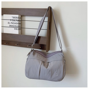 Detail of grey-purple nylon crossbody bag featuring zippered pockets on a wooden hanger
