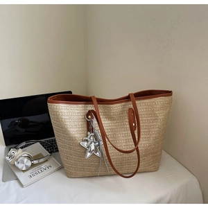 Detail der gewebten Strohtasche mit braunen Ledergriffen und silbernem Sternanhänger