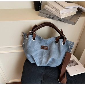 Detail of blue-grey tote bag with brown leather handles and adjustable fabric strap