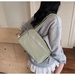 Side view of a light sage green nylon crossbody bag showing its size and texture on a model