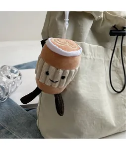 Détail d'un pendentif peluche tasse à café avec sourire brodé sur un sac beige