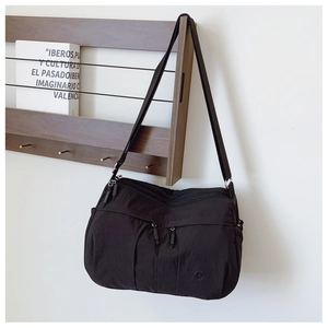 Detail view of black nylon crossbody bag featuring double front zippers on wood hanger