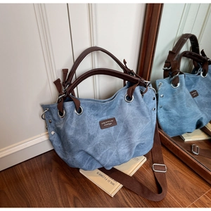Detail of blue textured tote bag featuring brown leather handles and silver metal grommets