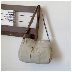 Detail of beige nylon crossbody bag with double front zippers on a wooden shelf
