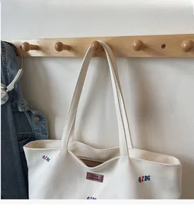 Detail of canvas tote bag with embroidered letters and leather logo on a wooden hook