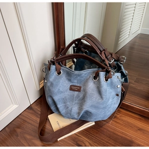 Detail of light blue canvas tote bag with brown leather straps and metal eyelets