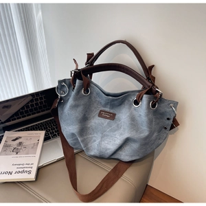 Detail showing washed blue fabric texture and leather handle on a large tote bag