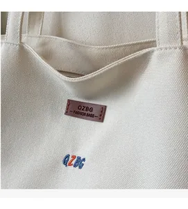 Detail of off-white canvas tote showing leather brand tag and colorful letter embroidery