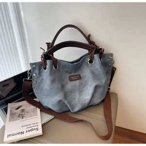 Detail of grey-blue canvas tote bag with brown leather tag and silver hardware