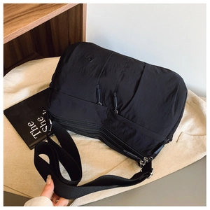 Detail view of black nylon crossbody bag with multi-zipper pockets and wide strap