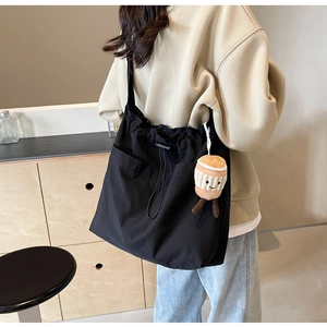 Détail d'un grand sac en nylon noir avec deux poches avant et un charm en peluche café
