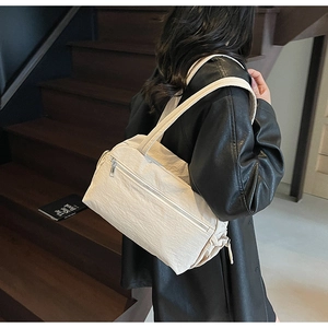 Detailed view of a beige nylon tote bag with pleated sides worn over the shoulder