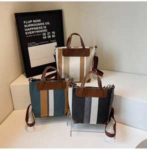 Three striped canvas tote bags with leather trim displayed on modern white geometric stands