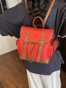 Red flap backpack with heart embroidery and brown faux leather straps in back view