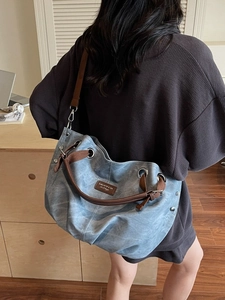 Large light blue tote bag with brown straps and rivets shown from a side-view on a model