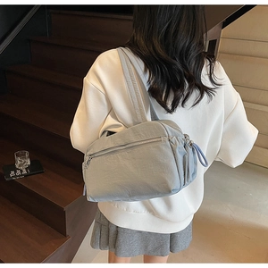 Detail of grey-blue nylon tote bag with drawstring side and wide shoulder strap on a model