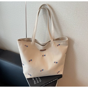 Close-up of beige canvas tote bag with blue embroidery and brown leather logo patch