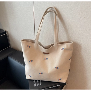 Detail of beige canvas tote bag with letter embroidery on a leather armchair