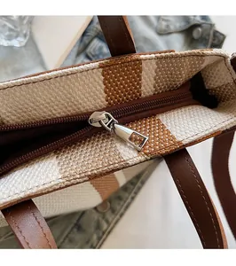 Detail of silver metal zipper and brown leather handle on a woven striped tote bag