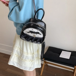 Detail showing bow decoration, lace trim and heart charm on a black and white mini backpack