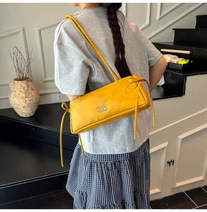 Détail d'un sac à bandoulière en cuir jaune vif avec logo métallique et nœud décoratif