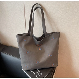 Close-up of deep grey canvas tote bag with embroidered letters and leather logo patch